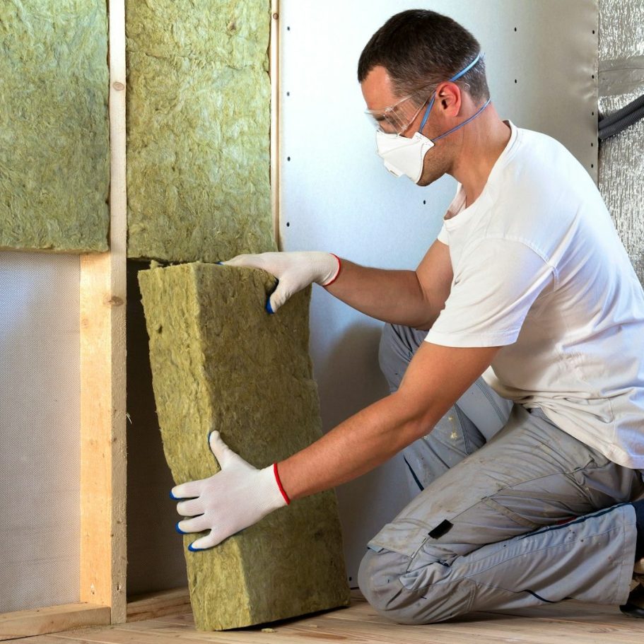 Mann in Schutzkleidung platziert Dämmmaterial in einer Wand, um den energetischen Zustand des Hauses zu verbessern.