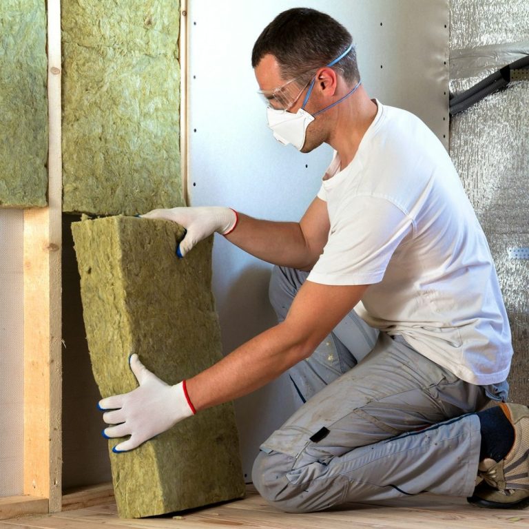 Handwerker in Schutzkleidung installiert Dämmmaterial zwischen Holzrahmen.