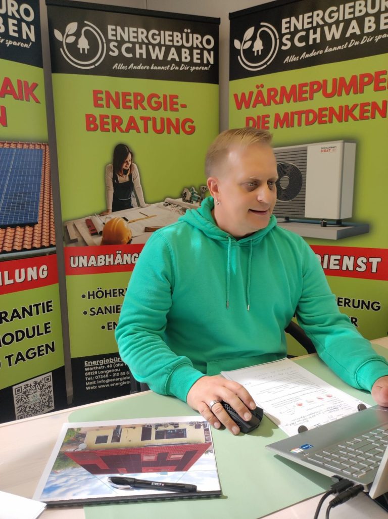 Michael Pelzer sitzt an einem Tisch, umgeben von Informationsplakaten zur Energiewende.