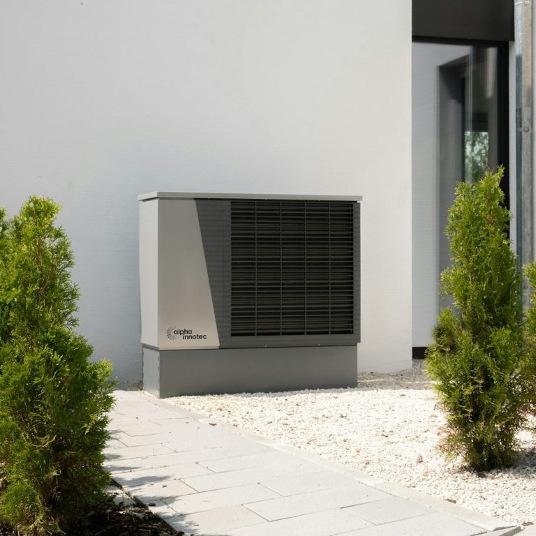 Wärmepumpe neben einem modernen Gebäude, umgeben von kleinen Pflanzen.