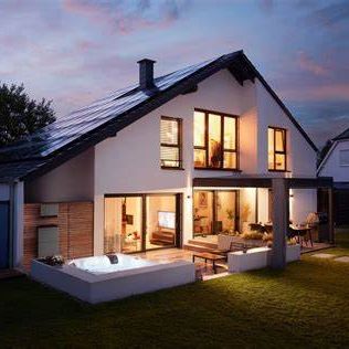 Modernes Haus mit Garten, großen Fenstern und einem Whirlpool im Freien. Auf dem Dach ist eine Photovoltaikanlage. Abenddämmerung.